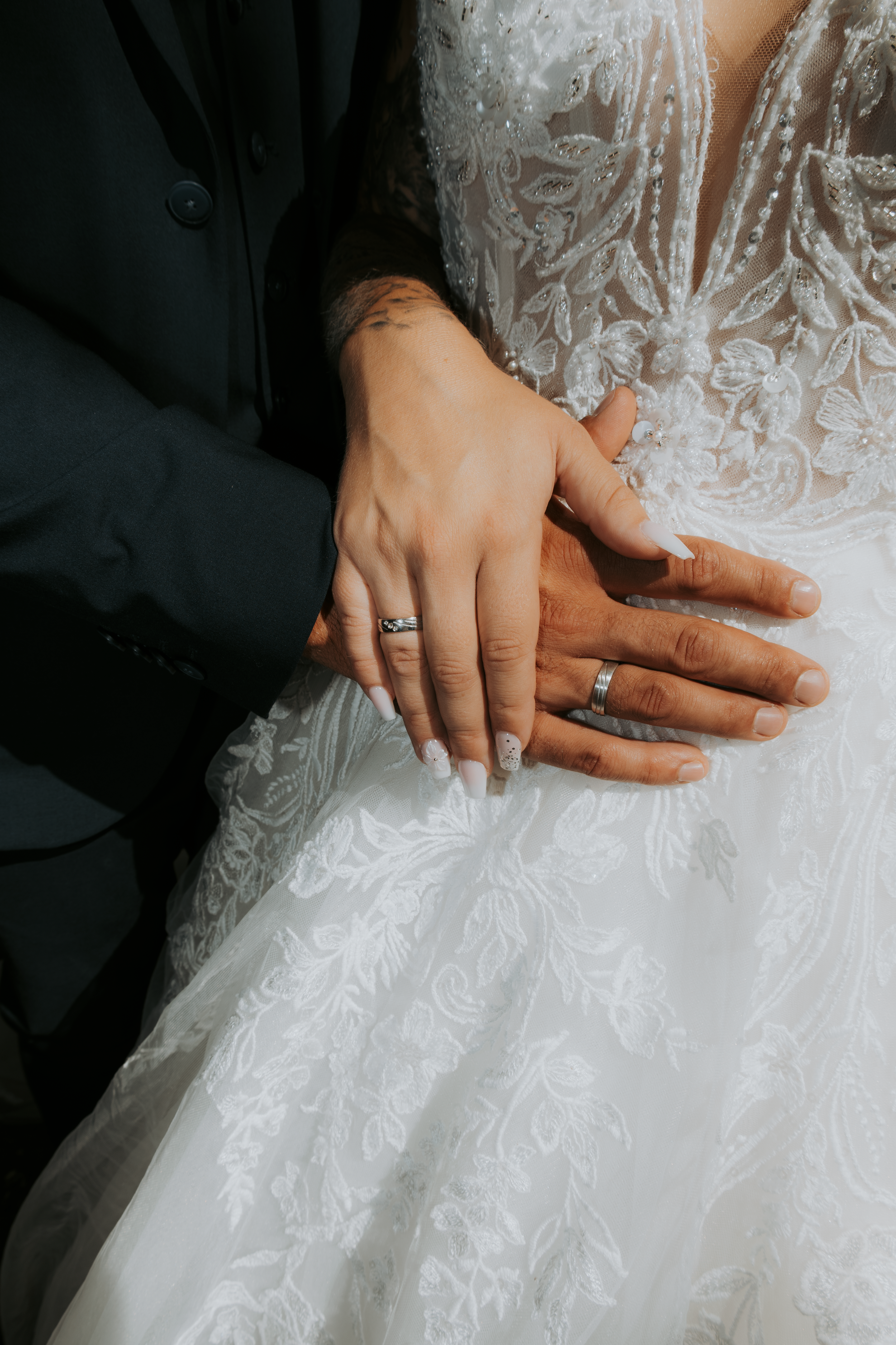 Bride and groom displaying wedding rings on white lace bridal gown, close-up detail shot.