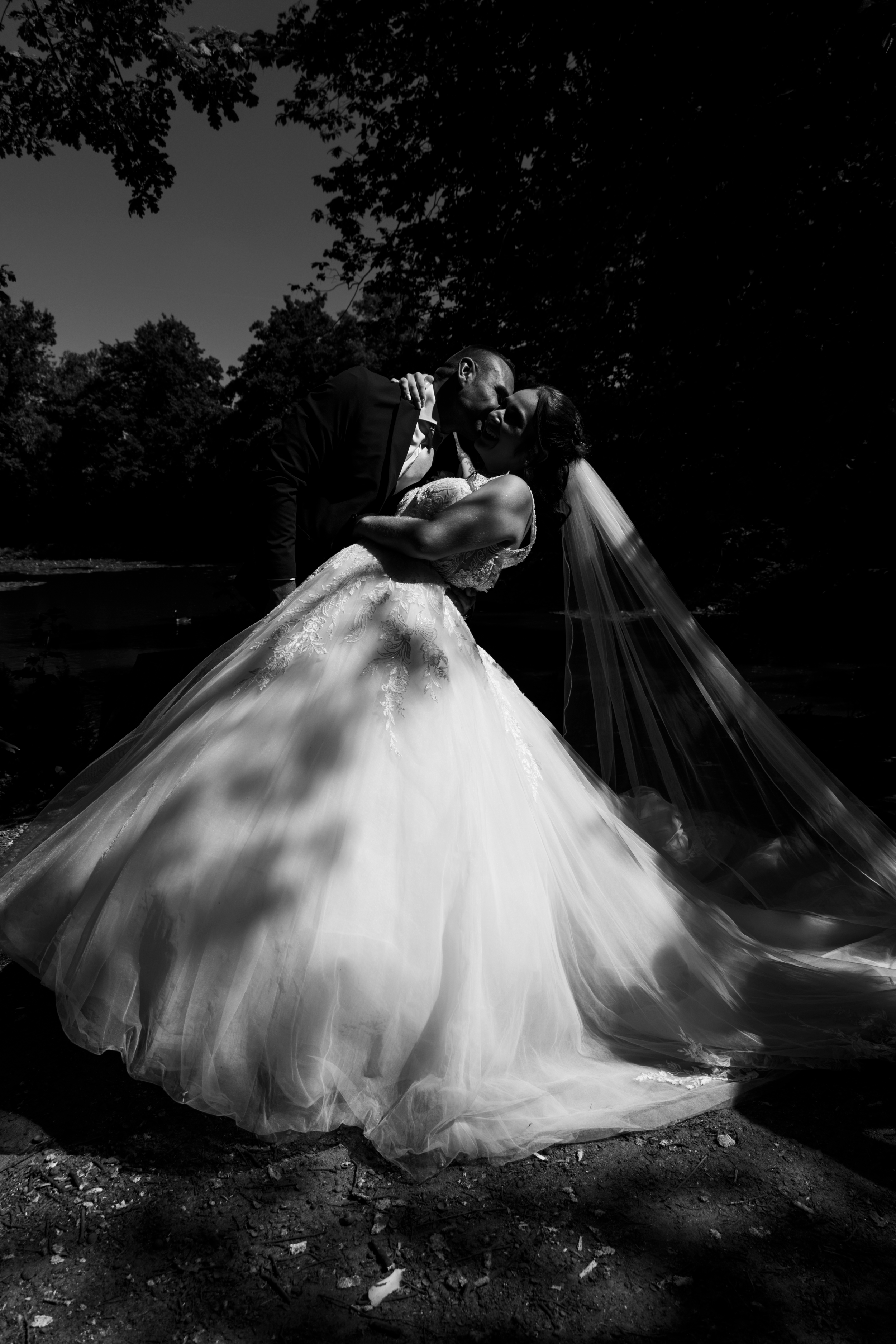 Black and white wedding photo of bride and groom sharing a romantic dip kiss outdoors, with flowing veil and ballgown.
