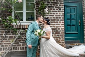 A romantic moment shared between newlyweds in front of a brick building with a teal door.