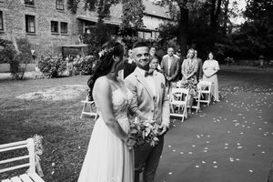 Black and white wedding ceremony photos show guests seated outdoors with flower petals scattered along the aisle.