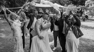 Wedding party dances joyfully in a garden setting during outdoor celebration.