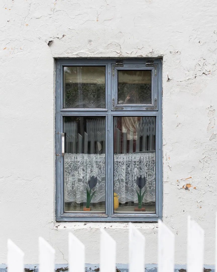 Old wooden window with peeling paint set into a textured white wall.