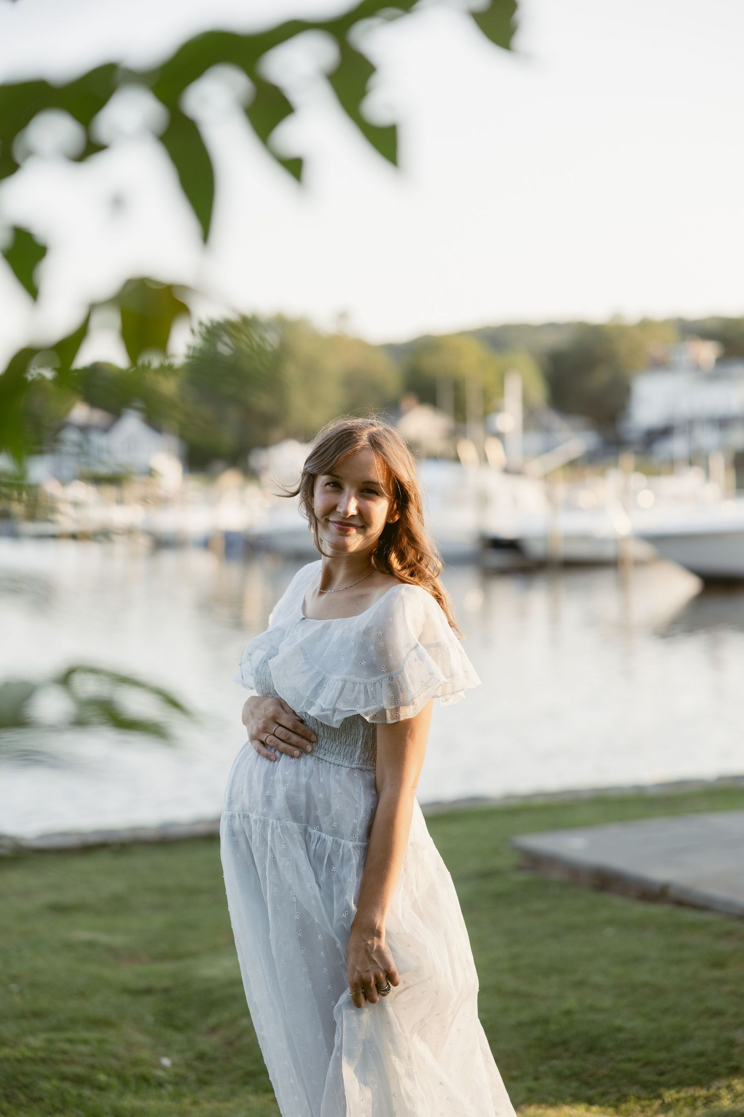 Girl in white lace dress playing by marina with boats in background.