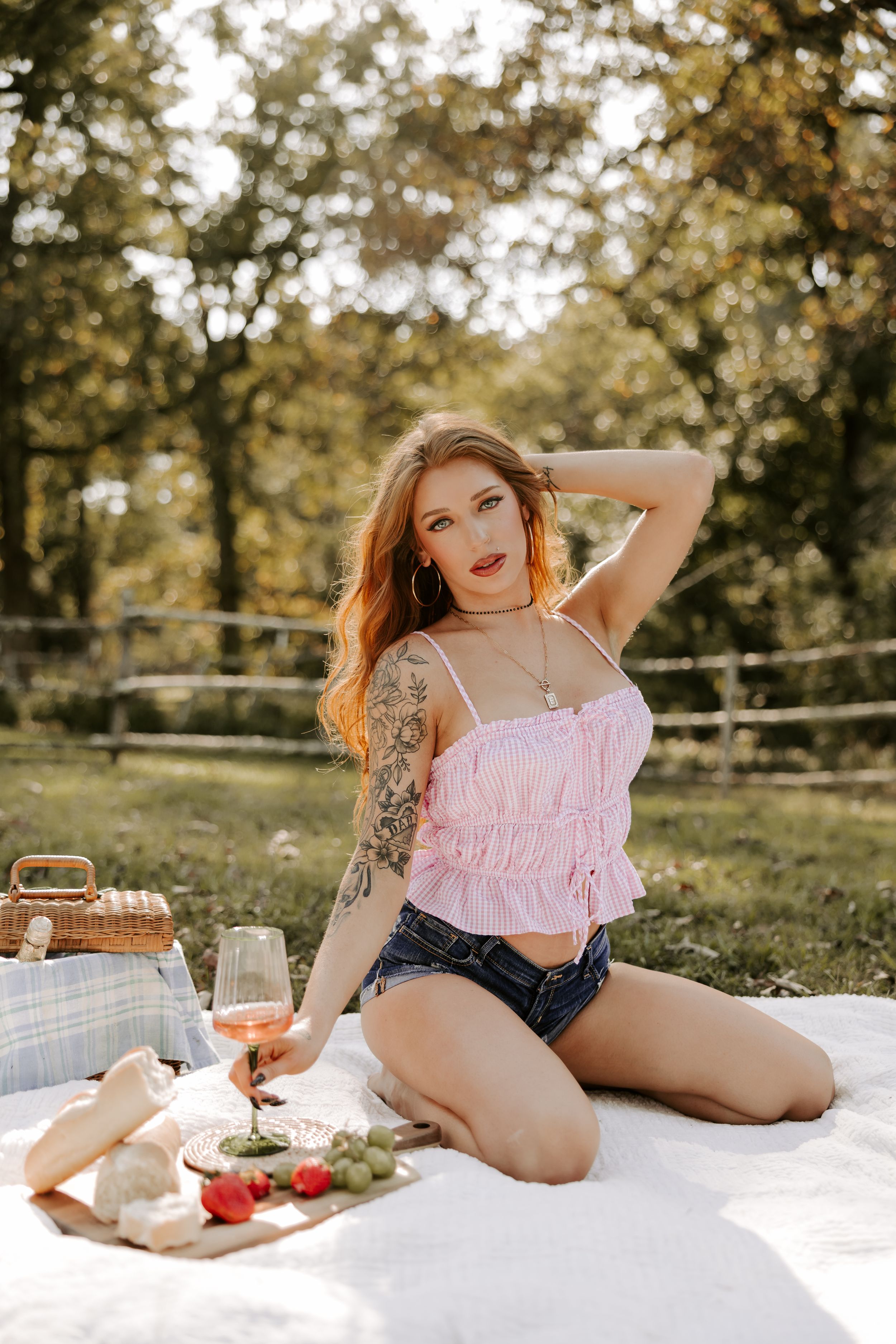 Summer picnic scene with model in pink top and denim shorts on white blanket with refreshments.