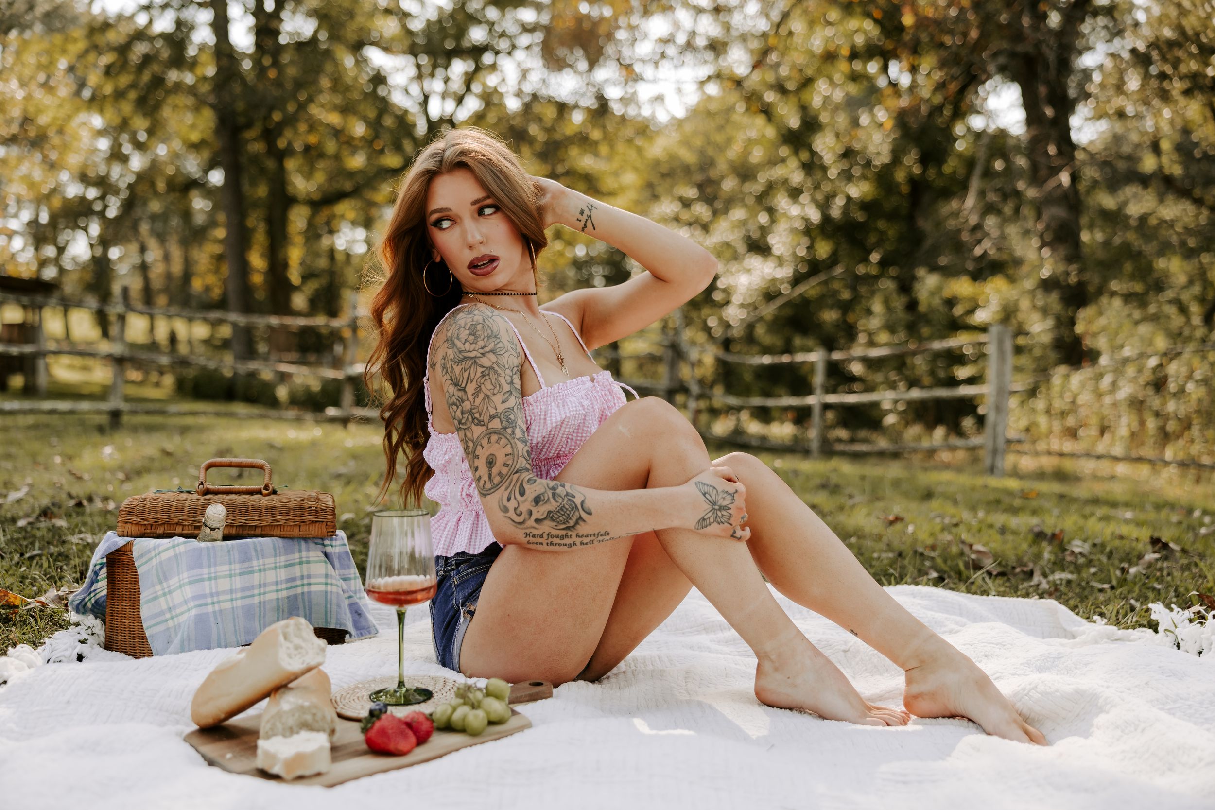 A picnic scene with wine, fruit, and a pink top against a sunny autumn backdrop in a park setting.
