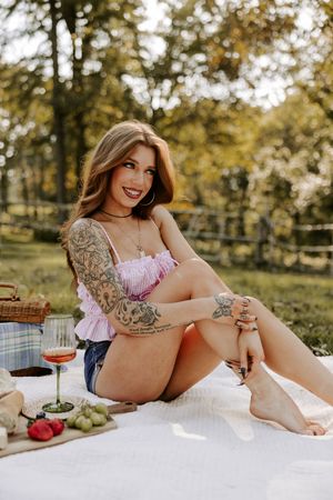 Sunny outdoor picnic scene with wine, fresh fruit, and decorative tattoo art.
