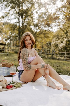 Summer picnic setup with wine and fresh fruit on white blanket in a park setting.