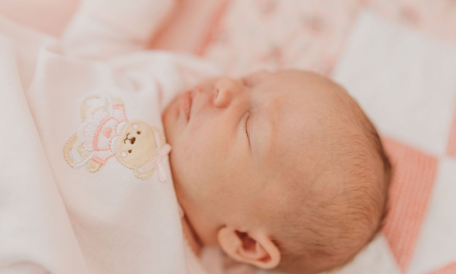 Peaceful sleeping newborn on soft pink bedding with delicate details.