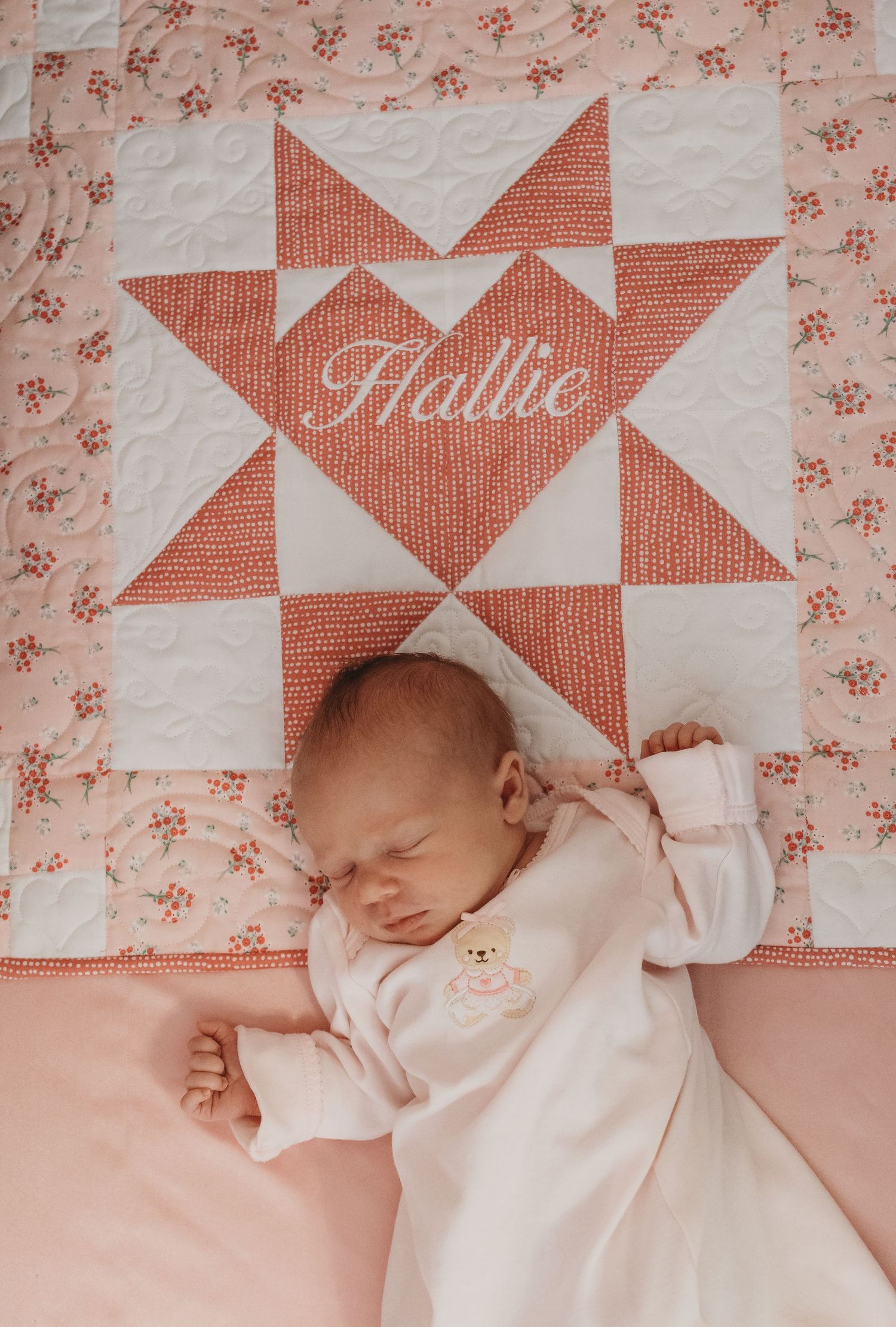 Newborn resting on geometric pink and white quilt with name embroidered.