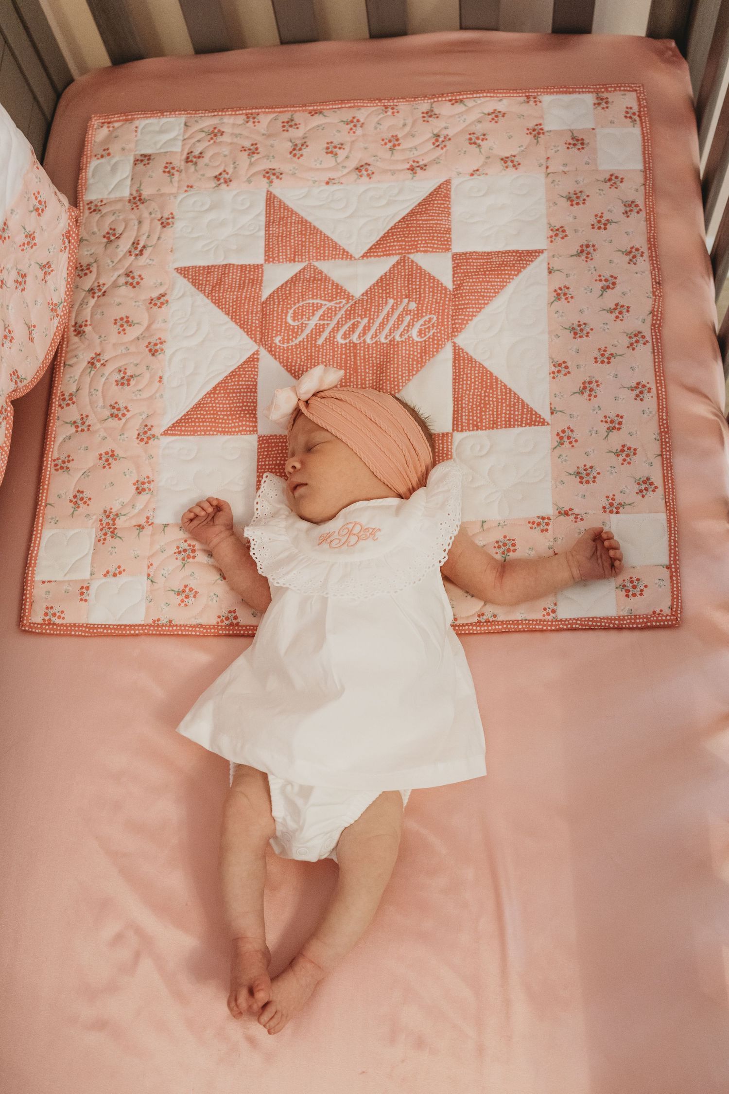Infant sleeping in wooden crib with pink bedding and decorative quilt.