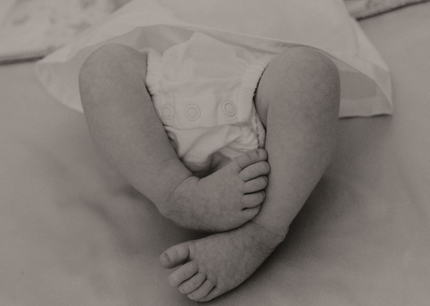 Black and white detail of infant feet against soft textured bedding.