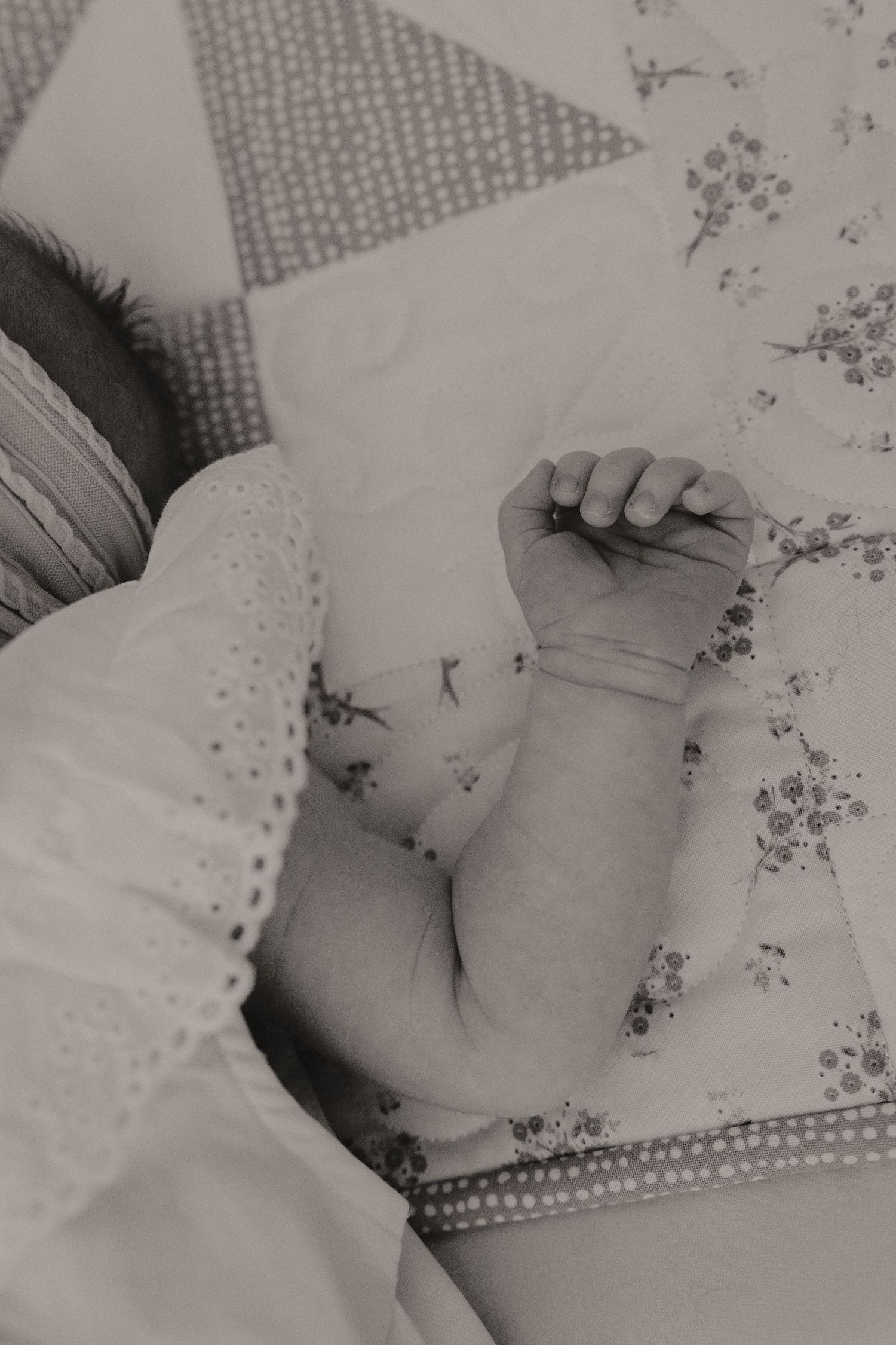 Black and white image of sleeping infant on floral patterned bedding.
