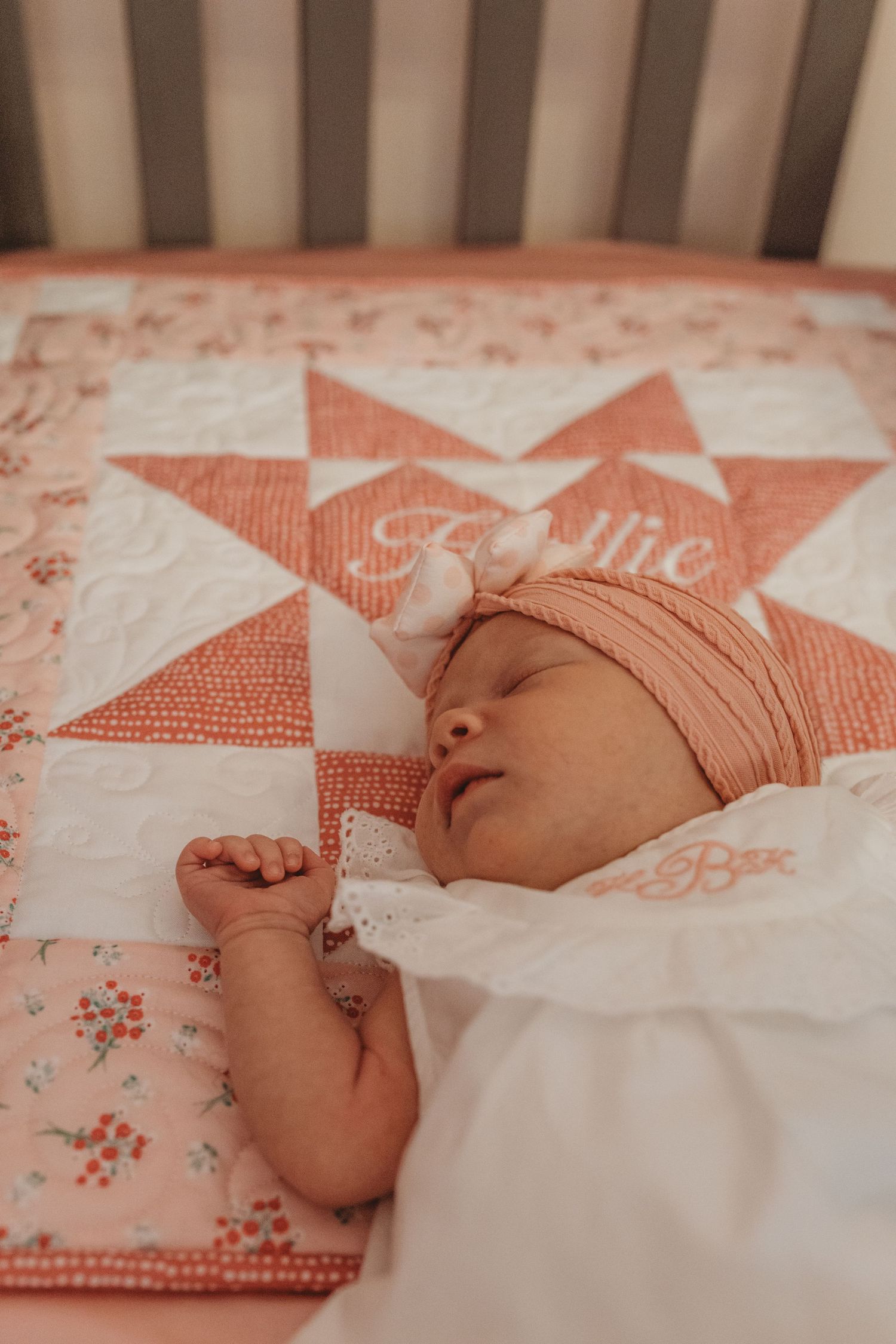 Baby resting in crib with peach-colored bedding and personalized quilt.