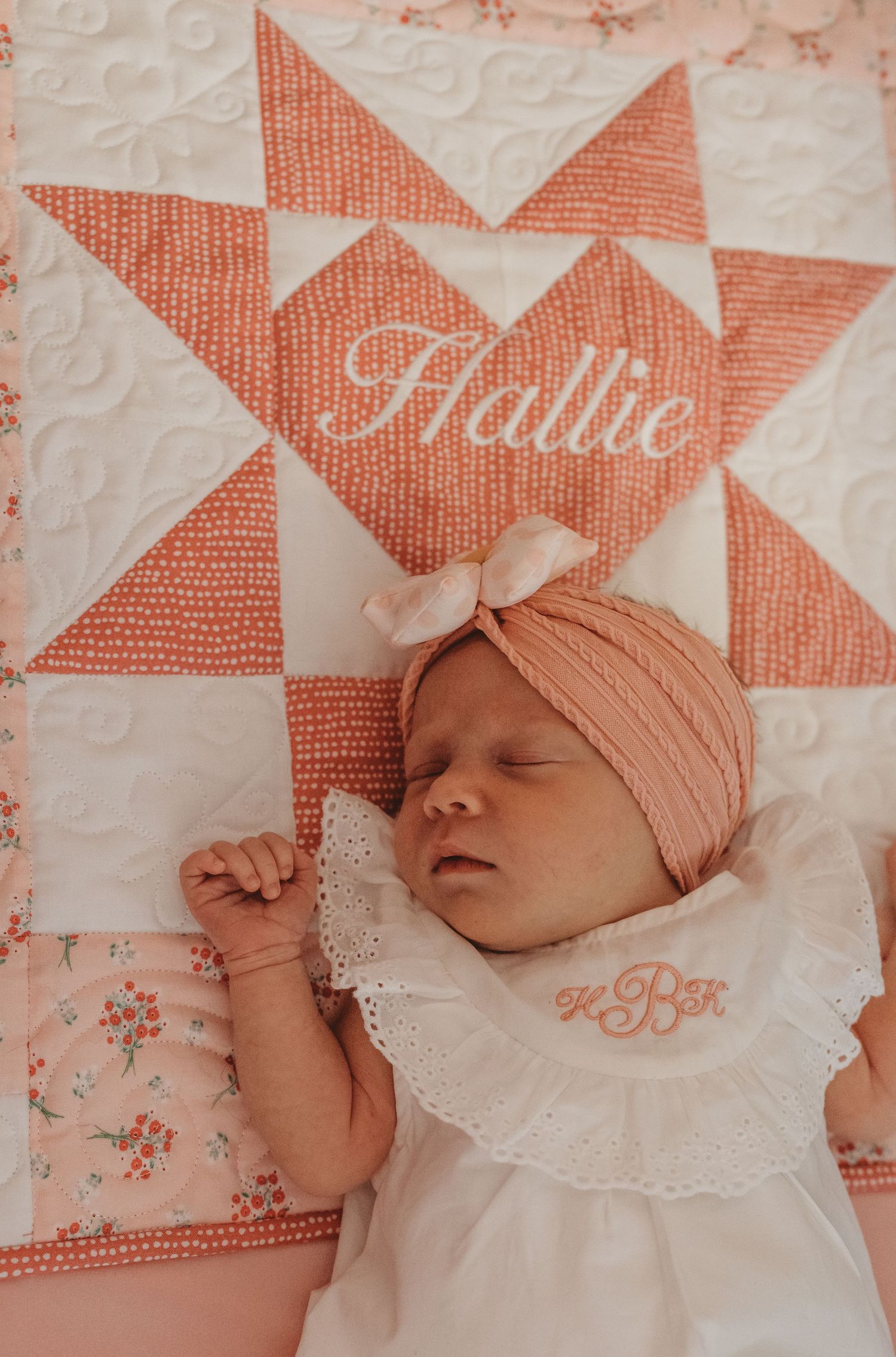 Sleeping infant on a peach and white star patterned quilt with lace trim detail.
