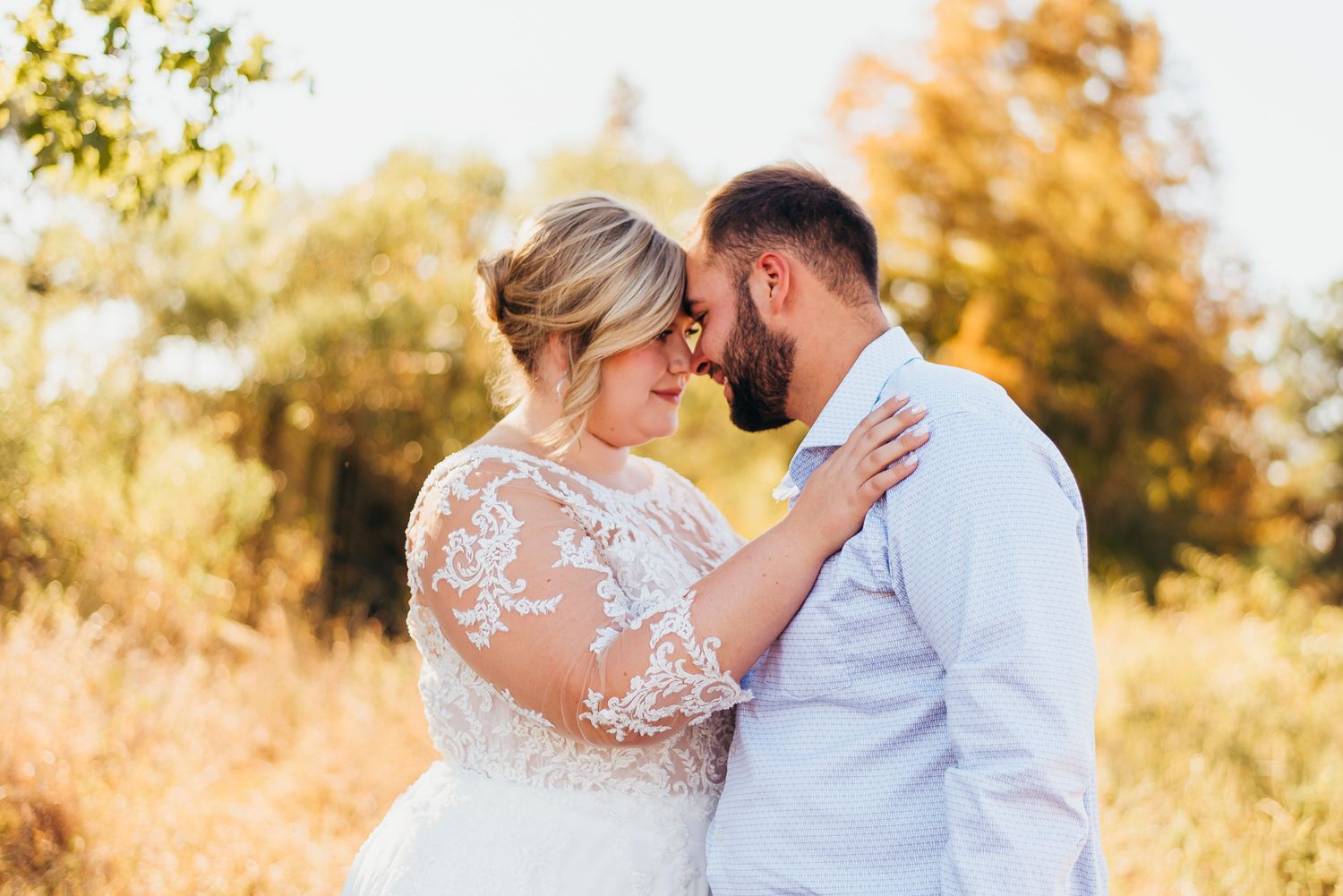 A romantic outdoor wedding moment with lace dress details against a golden autumn backdrop in warm sunlight.