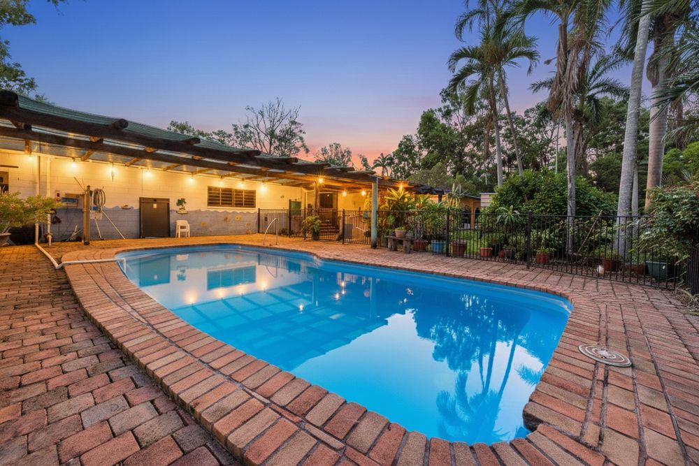 A curved swimming pool with brick paving and tropical landscaping illuminated at dusk creates a resort-like atmosphere.