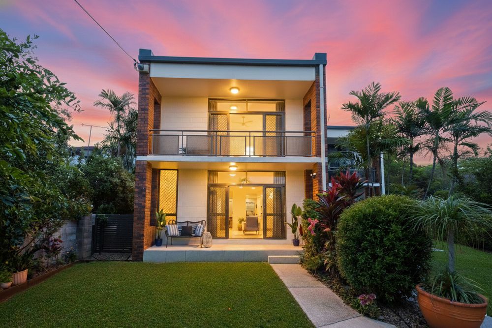 Modern luxury home exterior with glowing warm interior lights at sunset against pink and purple sky.