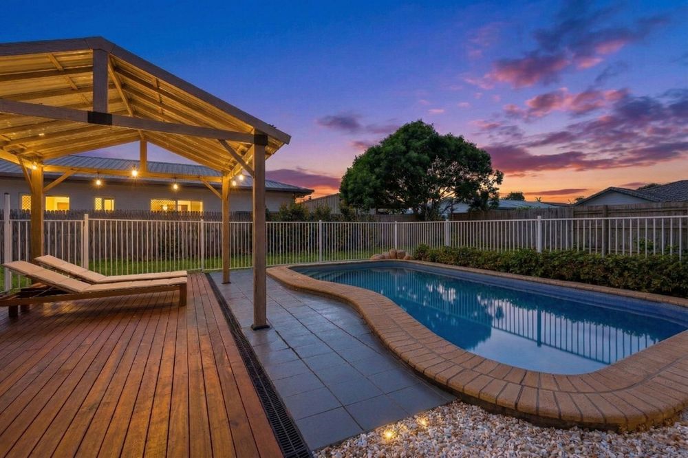 Illuminated covered deck and swimming pool at twilight with vibrant sunset colors reflecting in the still water.