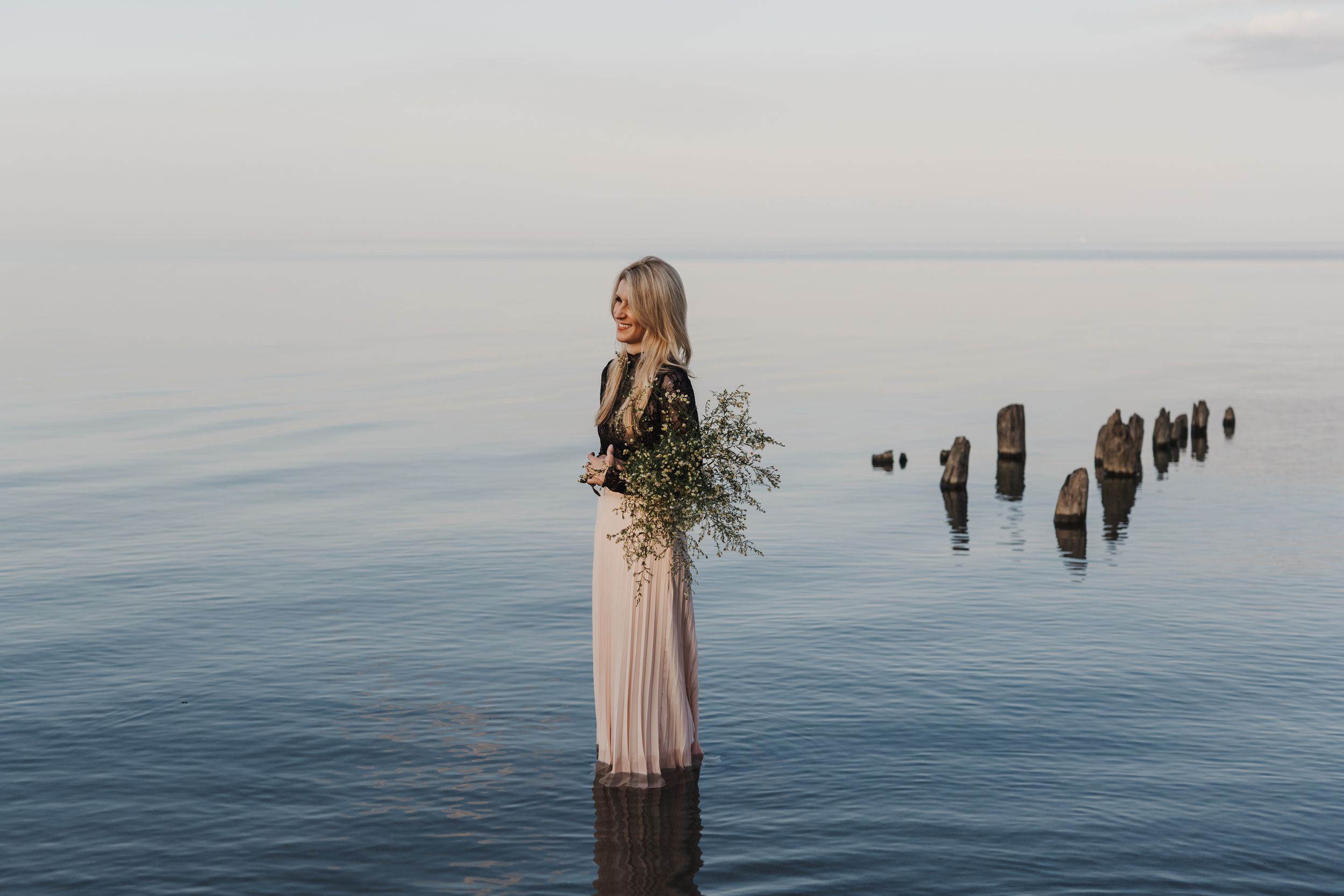 Michelle Hugill standing in calm lake water, holding a bouquet of wildflowers