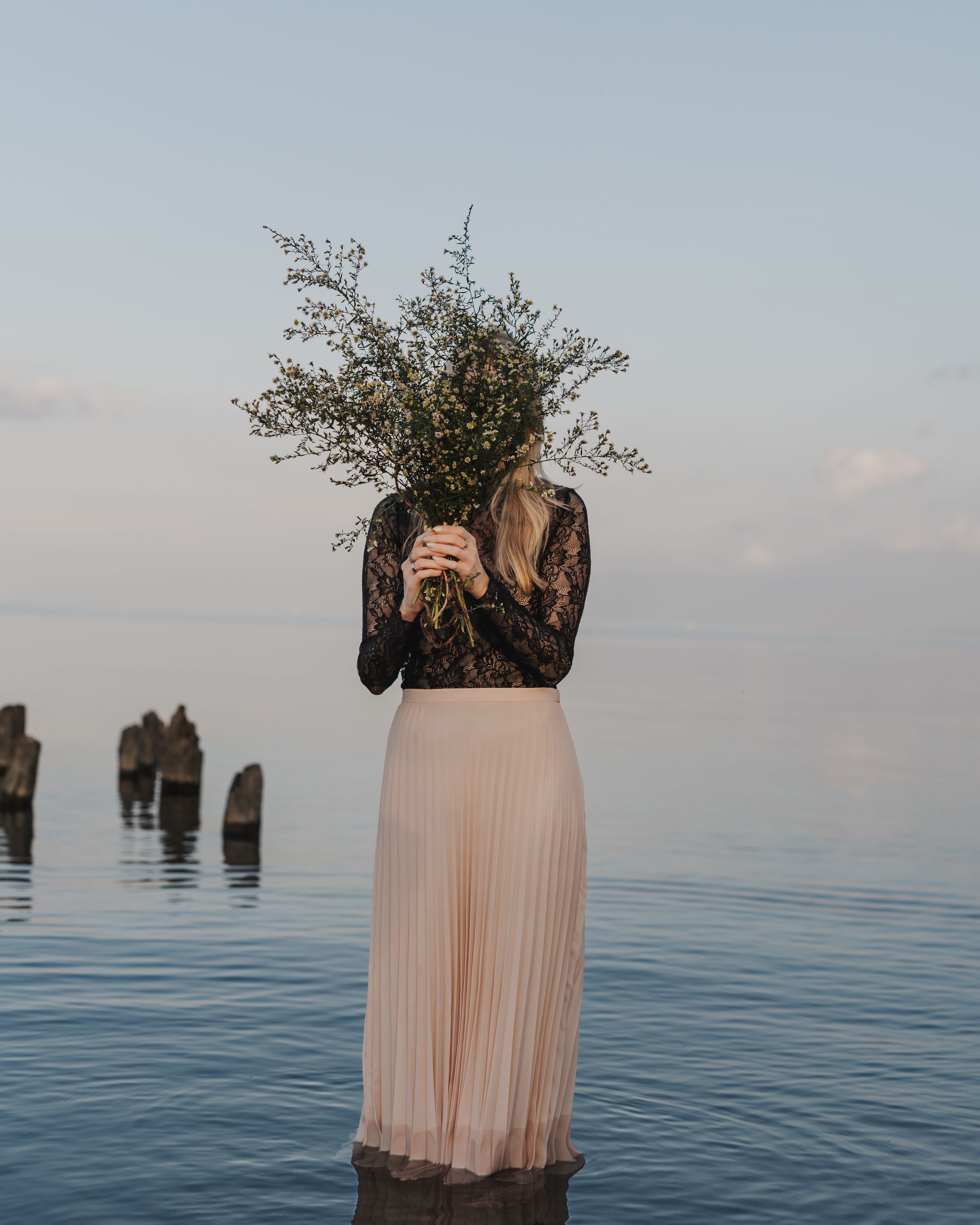 Michelle Hugill standing in calm lake water, holding a bouquet of wildflowers