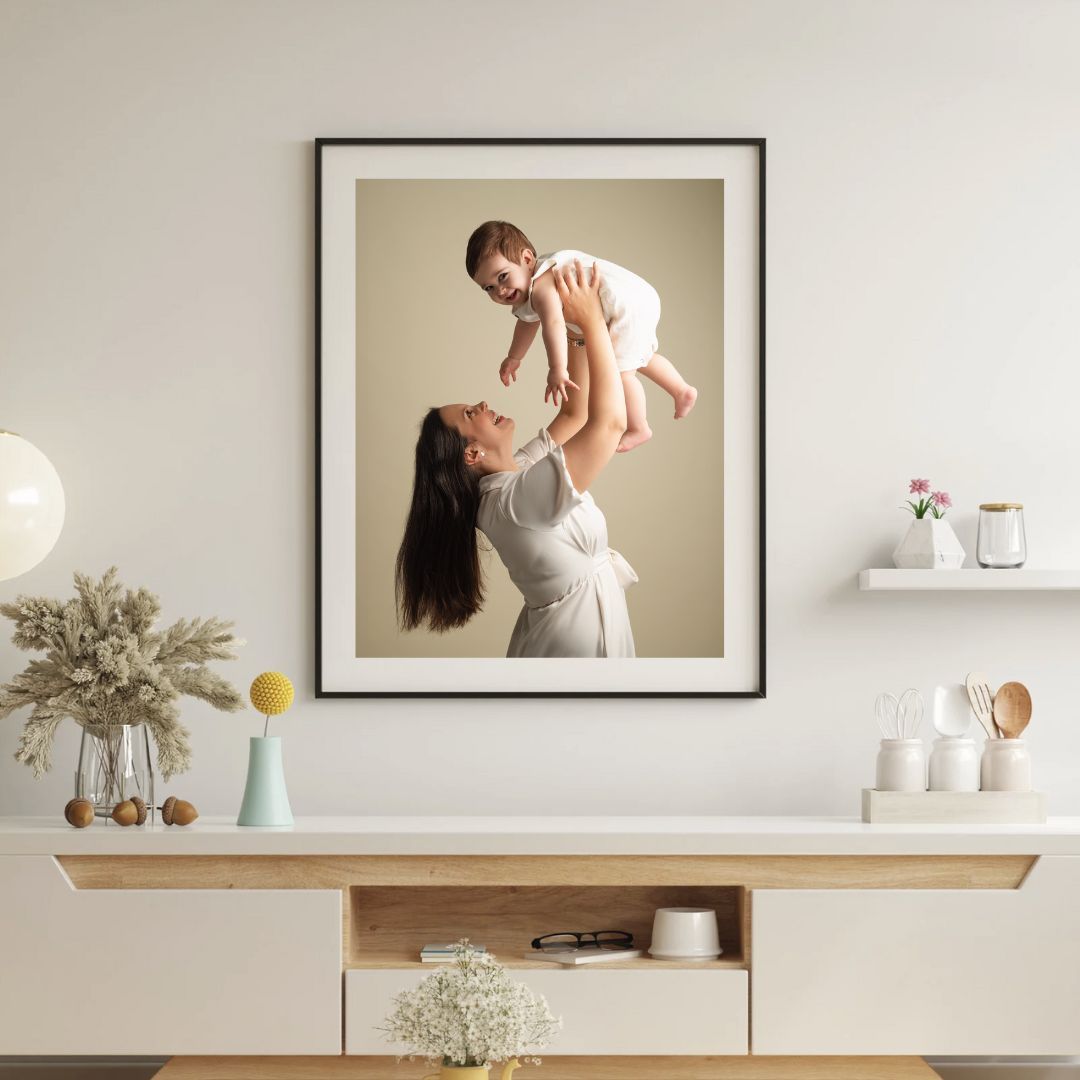 Framed photo of a mother lifting her baby displayed above a wooden sideboard in a modern home.