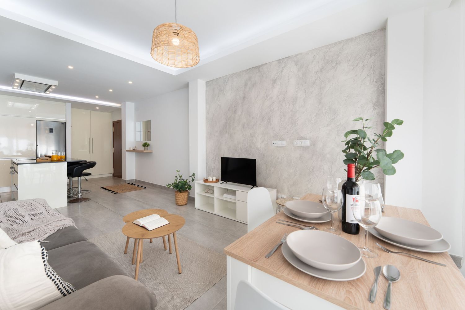 Modern minimalist apartment interior with white walls, grey furniture, and natural light flowing through large windows.