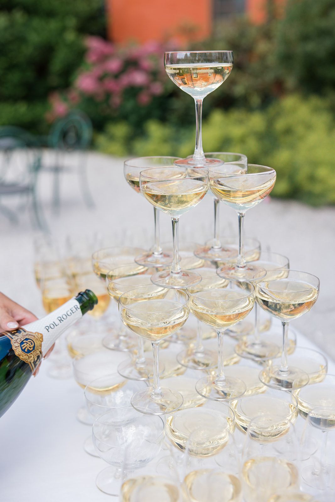 A pyramid of champagne glasses filled with sparkling wine stacked on a white tablecloth for a celebration.