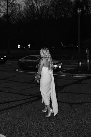 A couple walks together at night across a dark parking lot illuminated by distant lights.