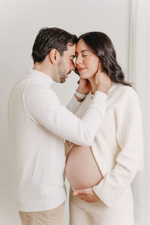 Couple attendant un enfant partageant un tendre moment les yeux clos, le futur papa pose amoureusement ses mains sur le cou de la maman
