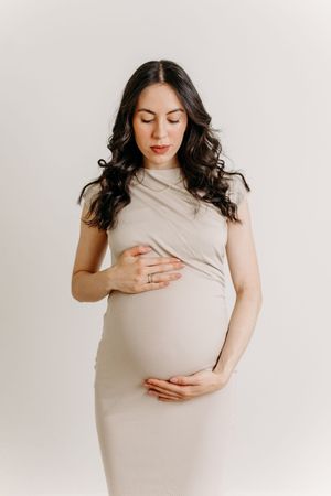 Future maman dans une robe moulante beige prenant la pose pour sa séance fine art de grossesse