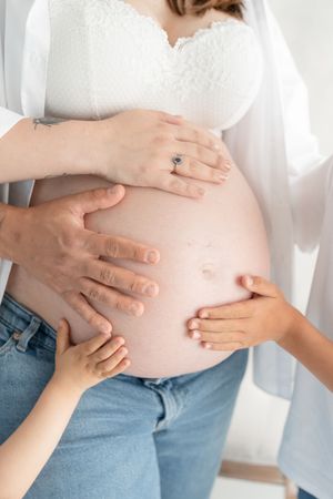 Plan rapproché sur le ventre d'une future maman avec la main du papa des celles des grands frères lors d'une séance maternité en famille