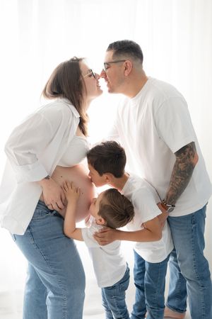 Famille en contre-jour attendant un nouveau bébé, les parents partagent un baiser et les grands frères font un bisou à la bedaine de maman