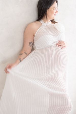 Plan rapproché sur une future maman qui tend le tulle de sa robe pour laisser voir son ventre rond à travers le tissu diaphane