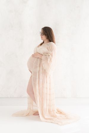 Profile plein pied d'une future maman au studio de Saint-Augustin dans une robe sable semi-transparente avec un arrière plan caneva fine art