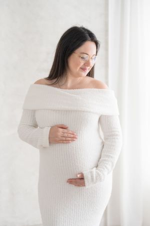 Portrait de grossesse fine art d’une future maman dans une robe blanche et douce au col bateau de la garde-robe du studio de Québec