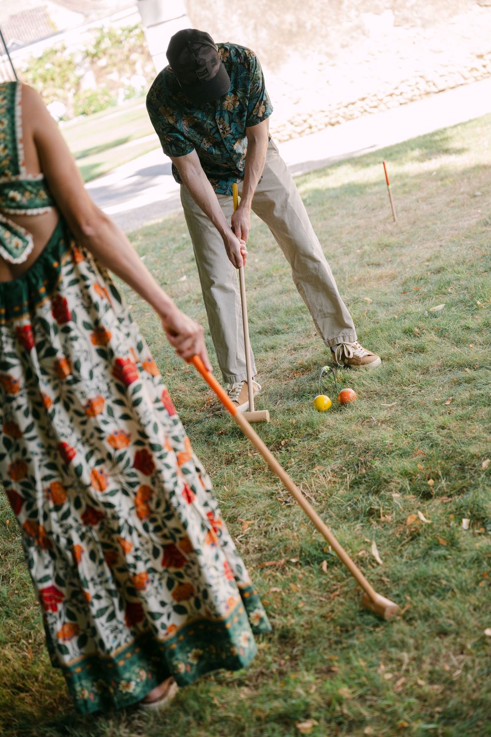 People playing croquet on a lawn with vintage floral dresses and wooden mallets.