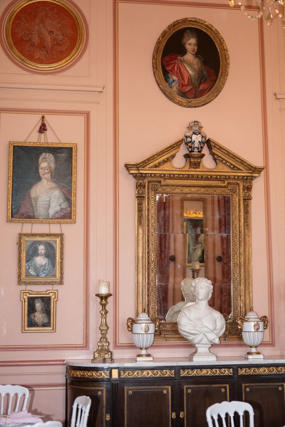 Elegant pink room with ornate gold-framed portraits and classical busts on display.