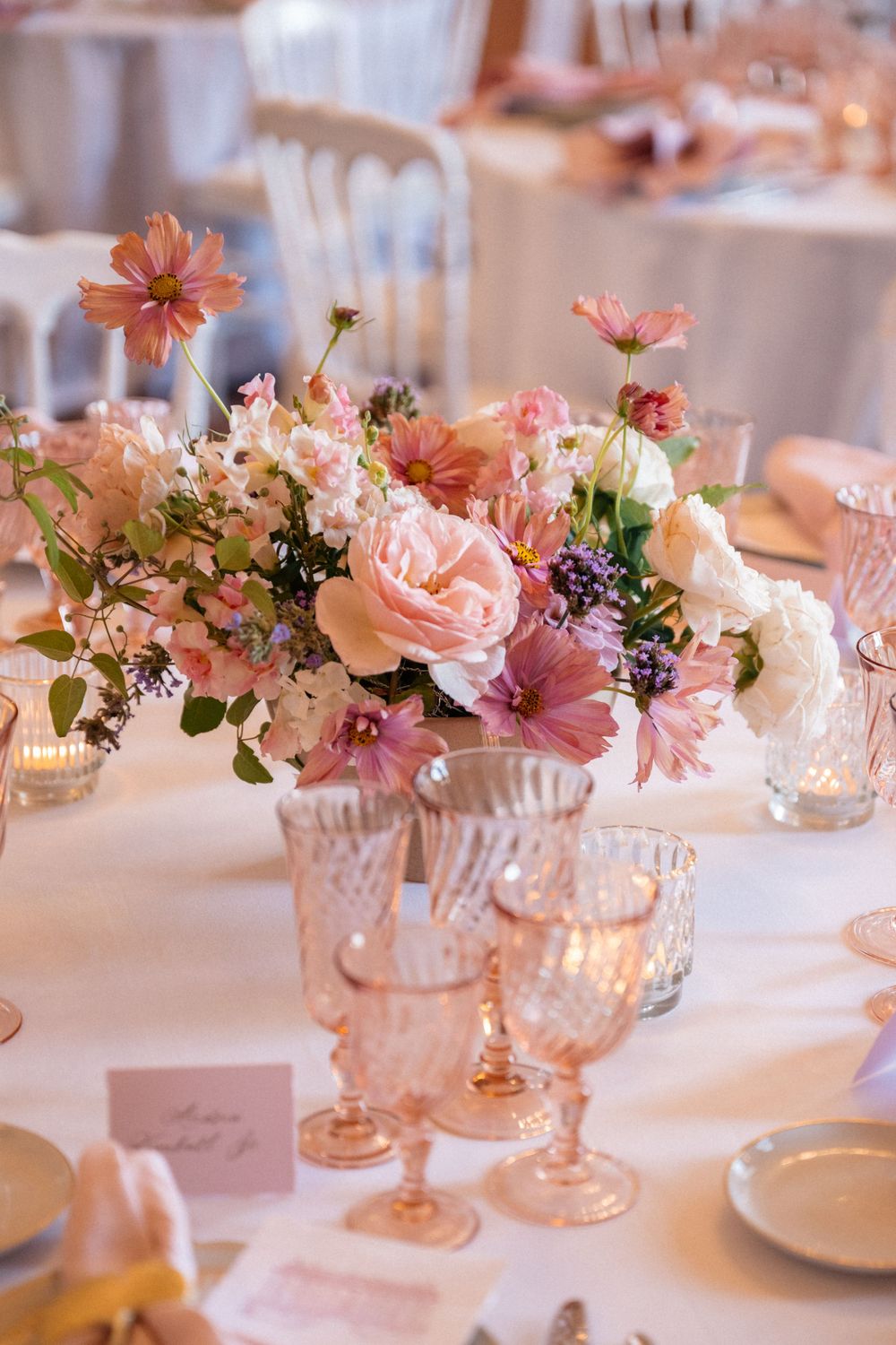 Elegant table setting with pink and peach floral centerpieces in crystal glasses and delicate place settings.