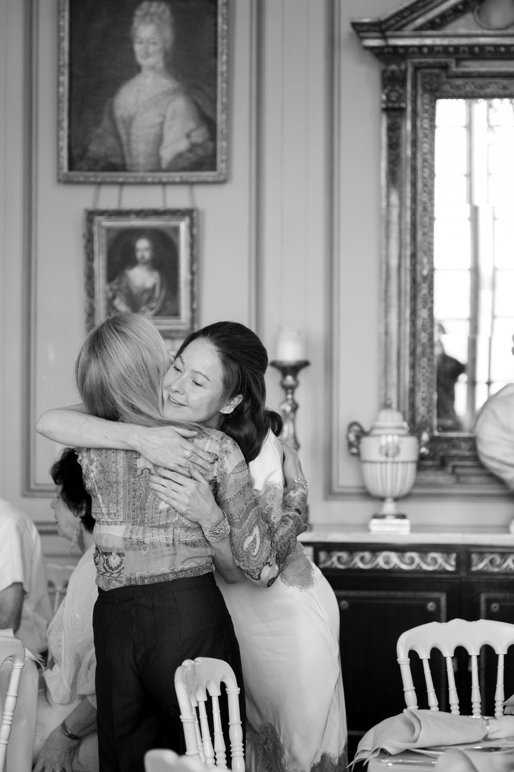 Black and white photo of people embracing in an ornate historic room with portraits on walls.