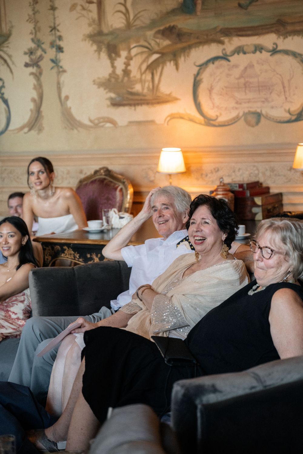 Wedding guests relaxing and laughing together on plush sofas in an ornately decorated room.