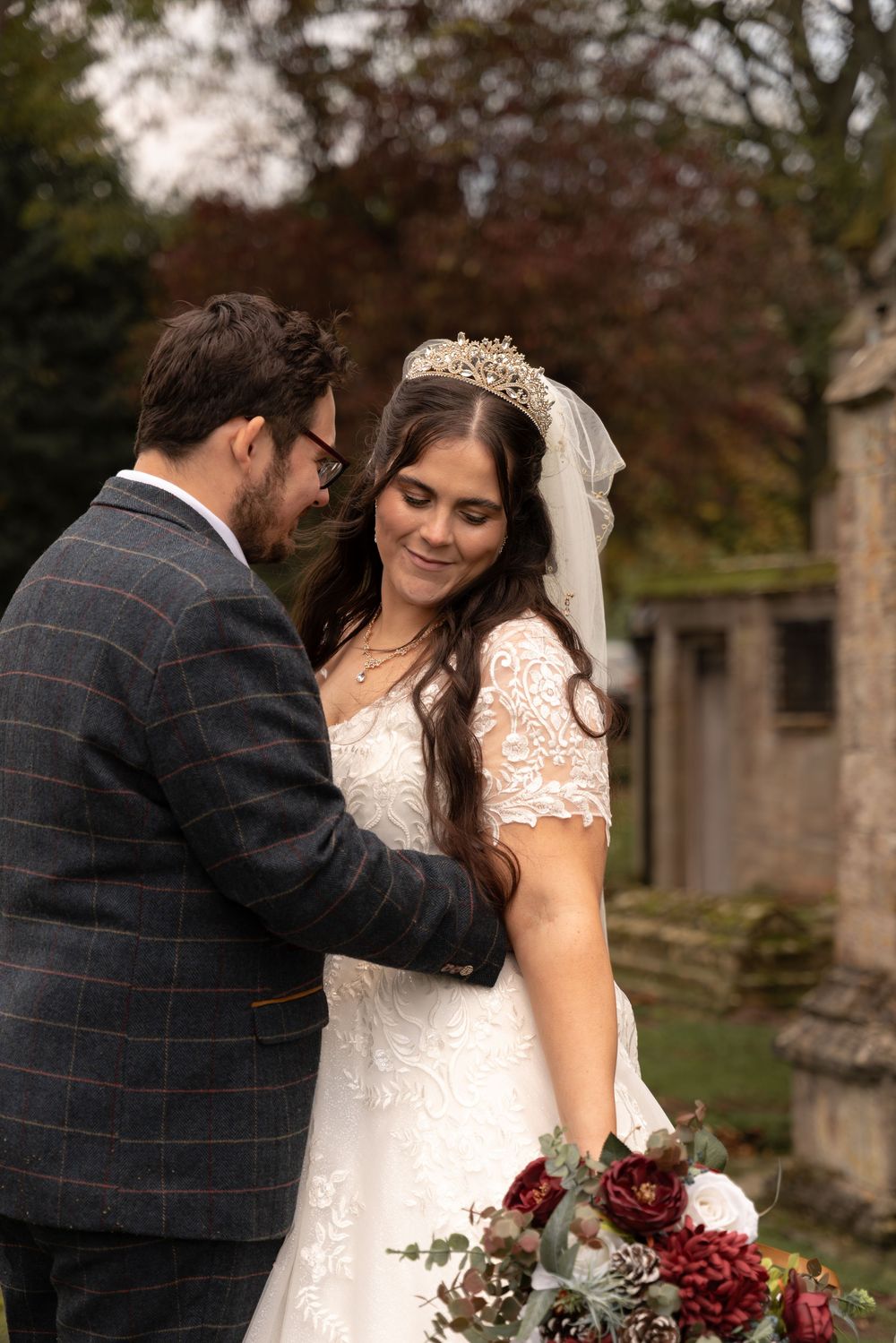 A romantic wedding couple shares tender moments in an autumn garden setting with burgundy floral accents.