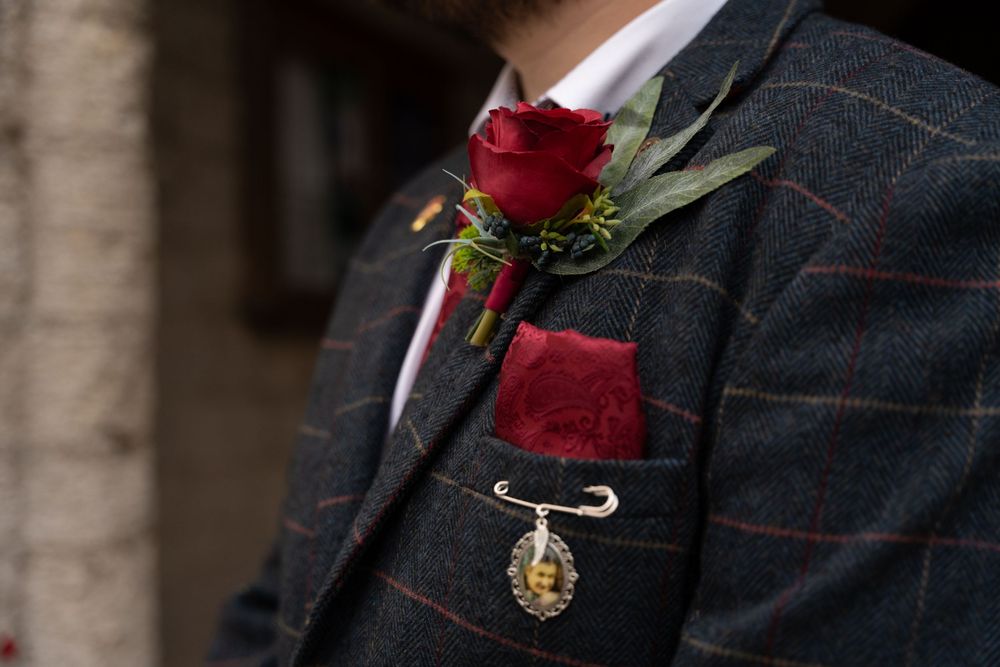 A dark navy suit jacket with a red rose boutonniere pinned to the lapel against a blurred background.