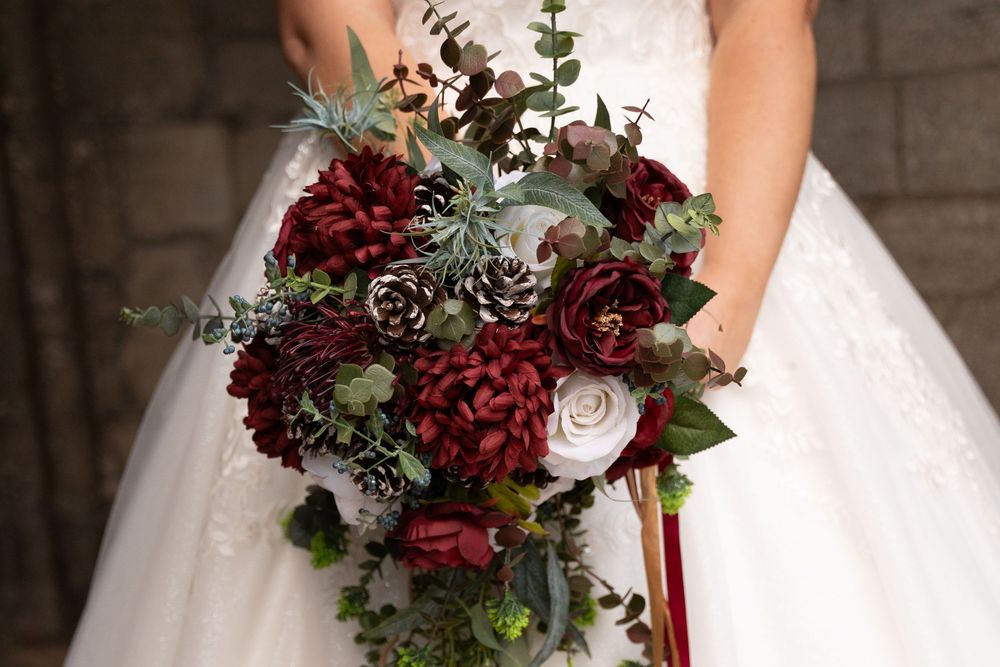 A romantic burgundy and white bridal bouquet with roses, dusty miller, and cascading ribbons for a winter wedding.