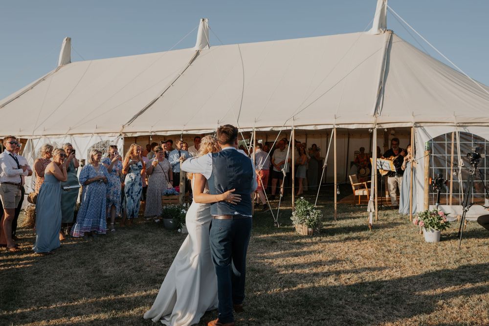 Newlyweds share romantic first dance outside a white wedding marquee surrounded by applauding guests.