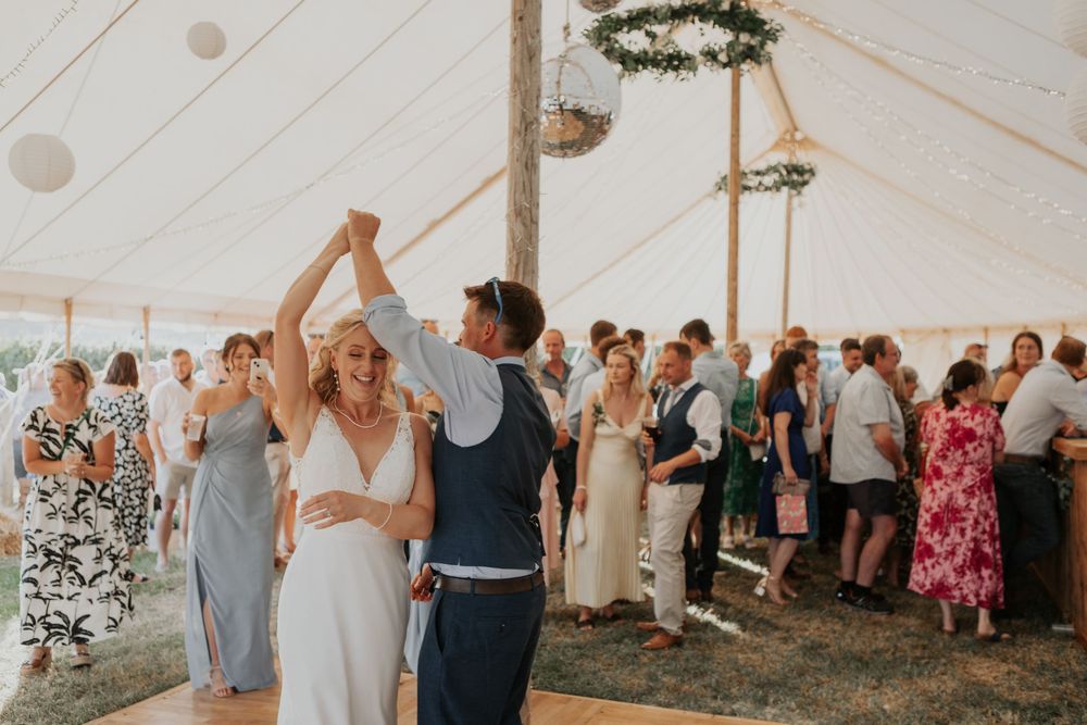 A bride and groom share a first dance under a decorated marquee tent at their wedding reception.