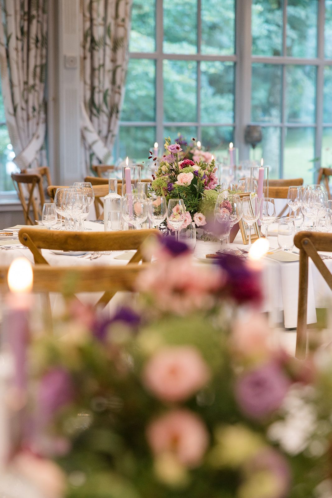 Elegant wedding reception table setting with pink and purple floral centerpieces in a bright sunlit venue.