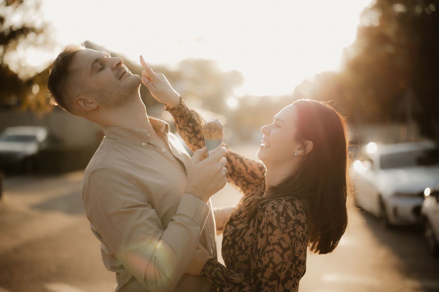 A playful couple sharing ice cream cones in warm sunset lighting.