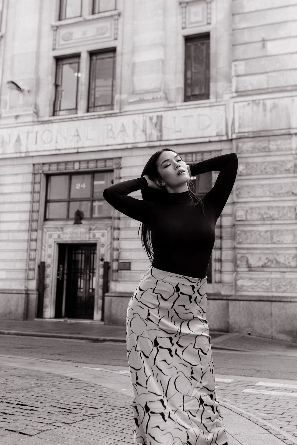 A dancer in a patterned dress performs an expressive sequence against a stone building facade.