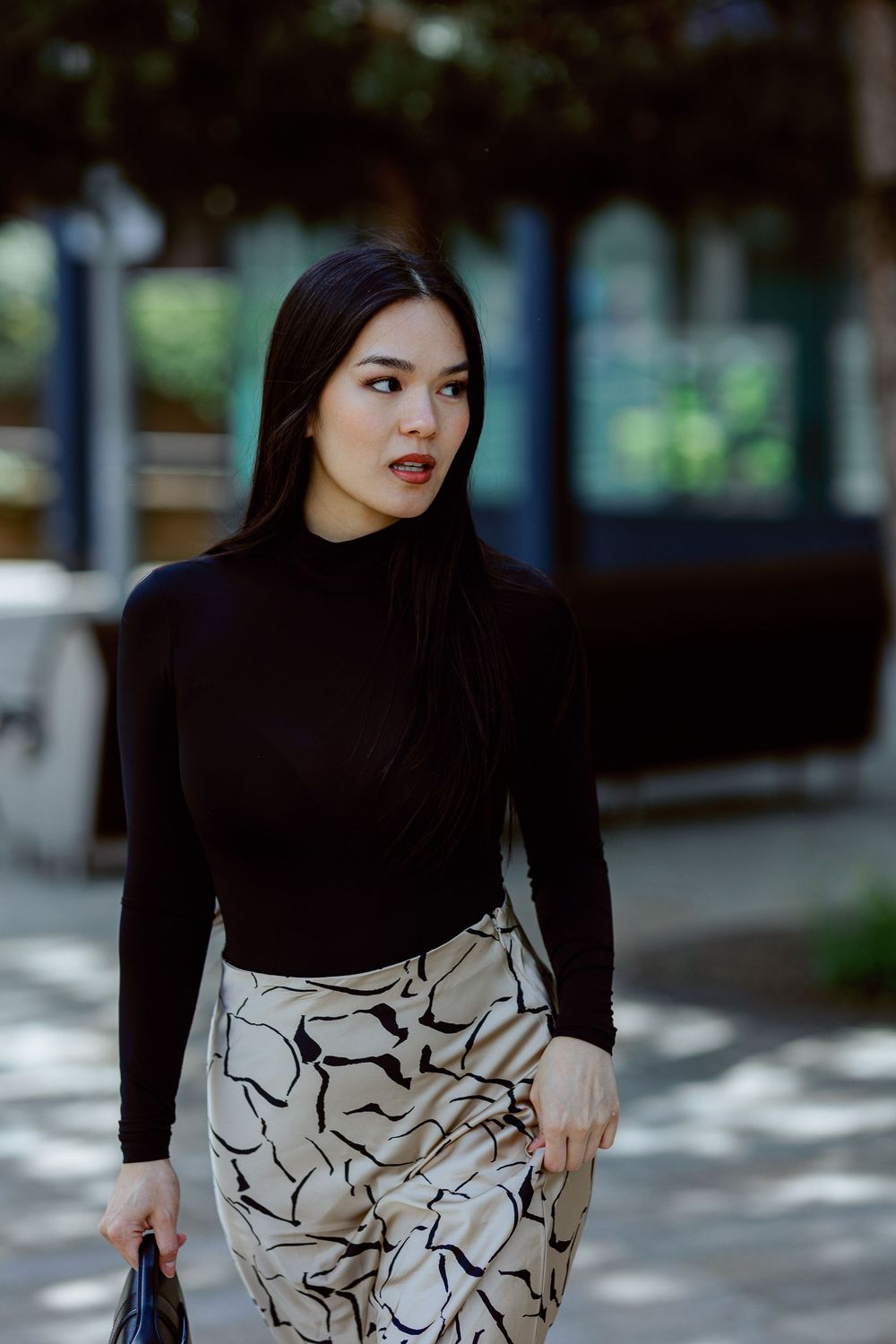 Stylish woman in black turtleneck and patterned pants poses outdoors on city street.