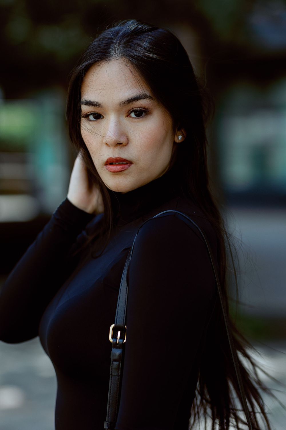 Portrait of someone in a black sweater with long dark hair against a blurred outdoor background.